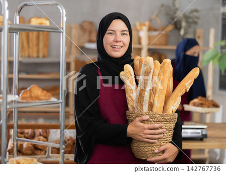 Young Muslim saleswoman displays baguettes while another seller working in background Young Muslim saleswoman displays baguettes while another seller working in background 142767736
