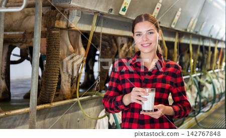 Female milker posing with glass of milk on dairy farm Female milker posing with glass of milk on dairy farm 142767848