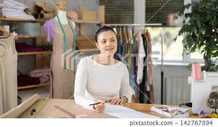Creative female seamstress designer drawing sketches on paper while sewing dress at workplace in fashion sewing workshop 142767894