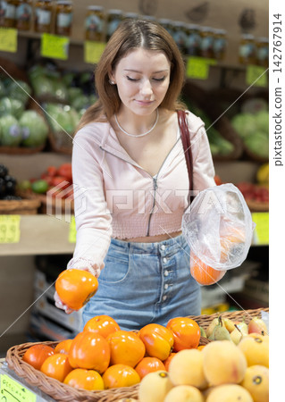 Woman choosing ripe persimmons in the store Woman choosing ripe persimmons in the store 142767914