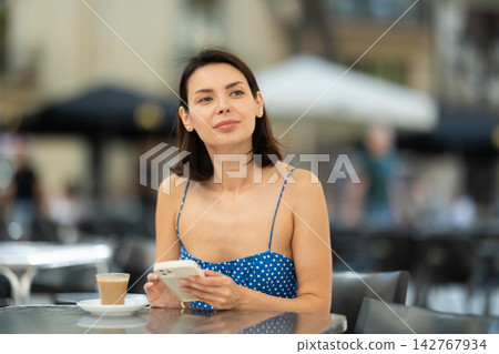 Young woman with phone drinking coffee in cafe Young woman with phone drinking coffee in cafe 142767934