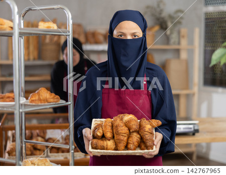 Portrait of girl seller of an oriental bakery in niqab, offering to buy fresh hot croissants 142767965