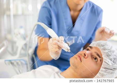 Young woman cosmetologist doing moisturizing procedure to young man Young woman cosmetologist doing moisturizing procedure to young man 142767985