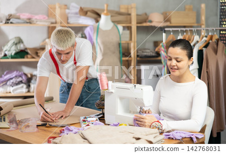 Asian seamstress sews on a machine next to a male fashion designer Asian seamstress sews on a machine next to a male fashion designer 142768031