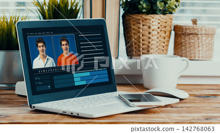 Using software to create a deep fake on a laptop at a desk with plants and a coffee cup nearby Using software to create a deep fake on a laptop at a desk with plants and a coffee cup nearby 142768063