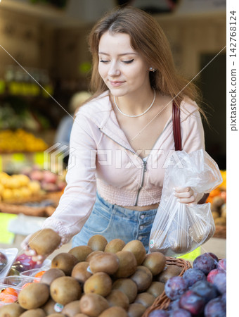 Young woman choosing ripe kiwi before weighing Young woman choosing ripe kiwi before weighing 142768124
