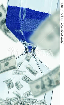 Hourglass filled with blue beads and falling dollar bills shows time and money concept Hourglass filled with blue beads and falling dollar bills shows time and money concept 142768189