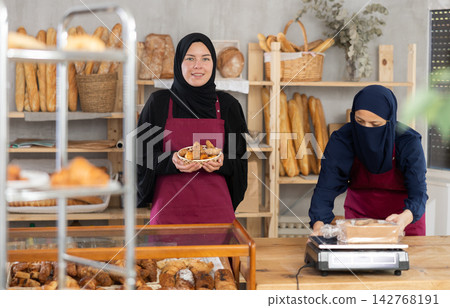 Smiling Muslim saleswoman presenting fresh pastries in bakery 142768191
