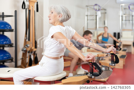 Senior woman performs Pilates exercises for weight loss and toning muscles of back and shoulders Senior woman performs Pilates exercises for weight loss and toning muscles of back and shoulders 142768305