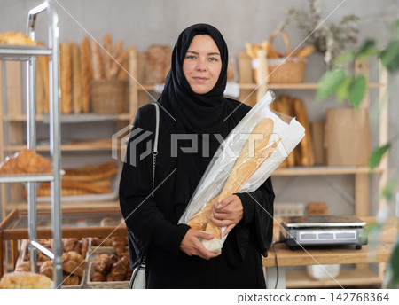 Woman in black hijab searching for fresh baked goods in bakery Woman in black hijab searching for fresh baked goods in bakery 142768364