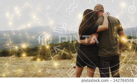 Couple standing together looking at a landscape with zodiac signs and stars in the sky Couple standing together looking at a landscape with zodiac signs and stars in the sky 142768508