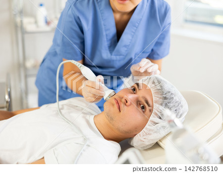 Young woman cosmetologist doing ultrasound procedure to young man Young woman cosmetologist doing ultrasound procedure to young man 142768510