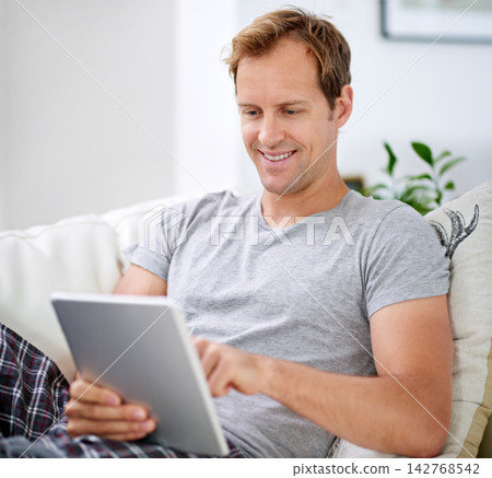 Man, tablet and morning reading or web ebook with internet connection, digital app or research. Male person, technology and online news on apartment sofa or article review for relax, smile or home Man, tablet and morning reading or web ebook with internet connection, digital app or research. Male person, technology and online news on apartment sofa or article review for relax, smile or home 142768542