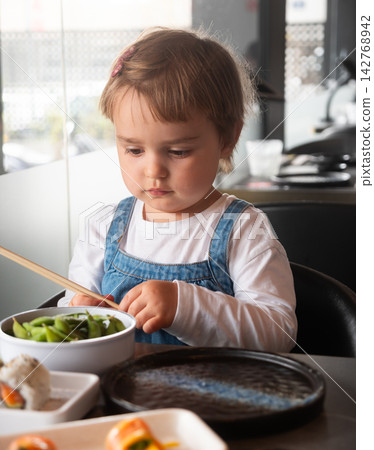 Child eating edamame at the table Child eating edamame at the table 142768942
