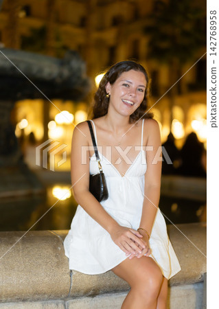 young woman sitting near a fountain in the evening young woman sitting near a fountain in the evening 142768958