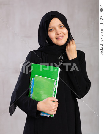Portrait of young woman in hijab holding stack of notebooks Portrait of young woman in hijab holding stack of notebooks 142769004