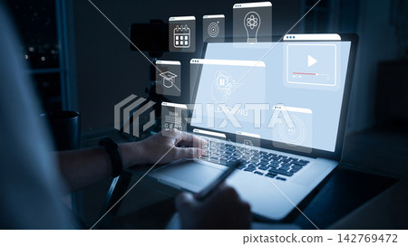 Person using a laptop to engage with e-learning content in a dimly lit room during evening hours Person using a laptop to engage with e-learning content in a dimly lit room during evening hours 142769472