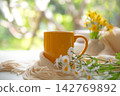 Coffee morning.  Yellow steaming cup of hot coffee for relax after working hobbies crochet on white wooden near window with flowers  142769892