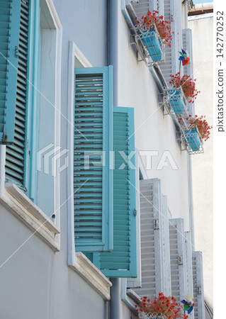 Shutters open on a building with flower pots in a sunny location Shutters open on a building with flower pots in a sunny location 142770252