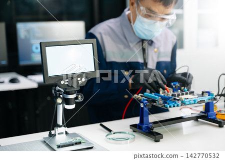 Skilled Asian engineer in safety gear tests a computer motherboard with a multimeter. Precision electronic repair and troubleshooting in a modern manufacturing laboratory. Skilled Asian engineer in safety gear tests a computer motherboard with a multimeter. Precision electronic repair and troubleshooting in a modern manufacturing laboratory. 142770532