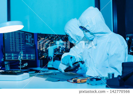 Cleanroom technicians in protective suits repairing a computer hard drive. Engineers conducting digital forensics and data recovery Cleanroom technicians in protective suits repairing a computer hard drive. Engineers conducting digital forensics and data recovery 142770566