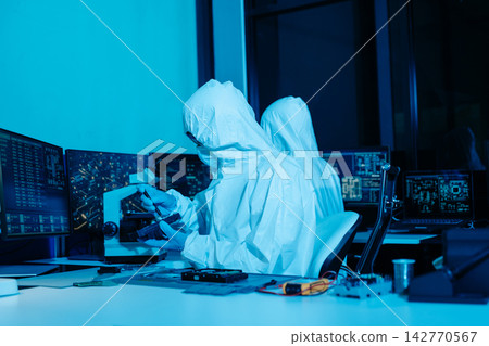 Cleanroom technicians in protective suits repairing a computer hard drive. Engineers conducting digital forensics and data recovery Cleanroom technicians in protective suits repairing a computer hard drive. Engineers conducting digital forensics and data recovery 142770567