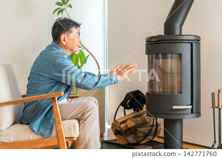 一位老人在燃木爐旁取暖。他享受著一種既能抵禦冬日嚴寒又能保持溫暖的生活方式。 一位老人在燃木爐旁取暖。他享受著一種既能抵禦冬日嚴寒又能保持溫暖的生活方式。 142771760
