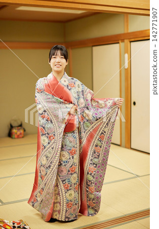 A young woman's smile as she tries on a high-quality, fully-dyed kimono. A young woman's smile as she tries on a high-quality, fully-dyed kimono. 142771907