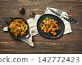 Pork stir fry served on black plates with herbs and spices in kitchen setting 142772423
