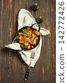 Pork stir fry served in bowl on wooden table with fork and napkin nearby 142772426