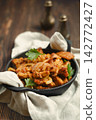 Pork stir fry with onions and herbs served in a cast iron skillet on wooden table 142772427