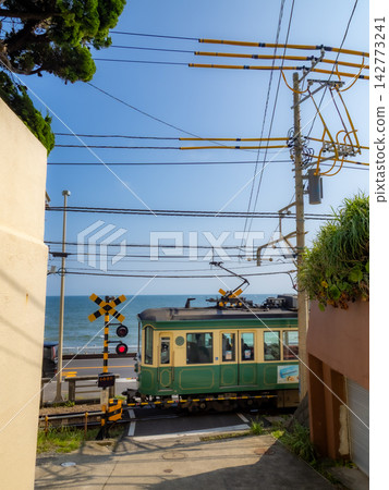 The Enoden train runs across the railroad crossing in front of Kamakura High School under a blue sky. The Enoden train runs across the railroad crossing in front of Kamakura High School under a blue sky. 142773241