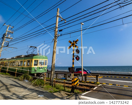 The Enoden train runs across the railroad crossing in front of Kamakura High School under a blue sky. The Enoden train runs across the railroad crossing in front of Kamakura High School under a blue sky. 142773242