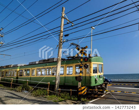 The Enoden train runs across the railroad crossing in front of Kamakura High School under a blue sky. The Enoden train runs across the railroad crossing in front of Kamakura High School under a blue sky. 142773243