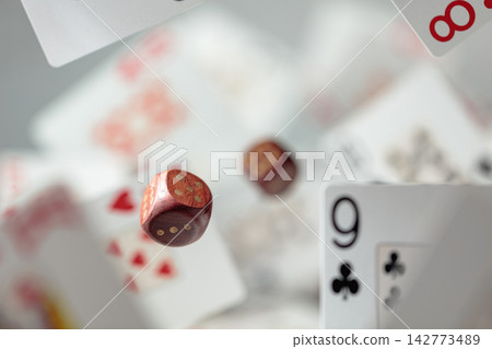 Wooden die in motion surrounded by playing cards. 142773489