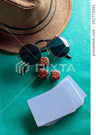 Playing cards, wooden dice, sunglasses and a hat on a green cloth. 142773491