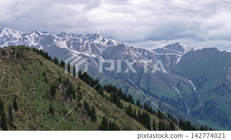 Snow-capped mountains and green hills under cloudy sky in Central Asia 142774021