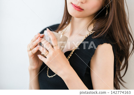 一位女士手持一杯飲品，悠閒地放鬆著。她佩戴的精緻首飾，包括一枚戒指和一條項鍊，十分引人注目。 142774163