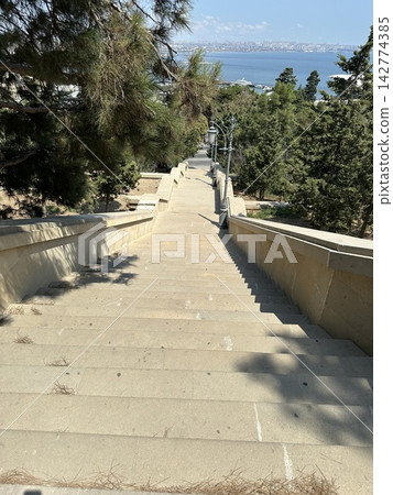 Wide concrete staircase leading through a green tree lined park pathway in summer. Stairs in the park. Wide concrete staircase leading through a green tree lined park pathway in summer. Stairs in the park. 142774385