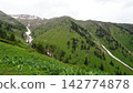Lush green mountain landscape with snow-capped peaks in the background Lush green mountain landscape with snow-capped peaks in the background 142774878