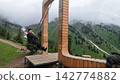 Person on wooden swing in mountainous landscape with cloudy sky Person on wooden swing in mountainous landscape with cloudy sky 142774882