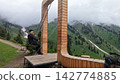 Man sitting on swing in wooden arch structure overlooking mountains Man sitting on swing in wooden arch structure overlooking mountains 142774885