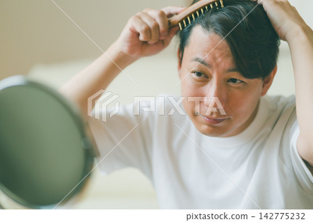 一位四十多歲的男士正在照鏡子檢查頭皮,準備開始他的頭髮護理。 一位四十多歲的男士正在照鏡子檢查頭皮,準備開始他的頭髮護理。 142775232