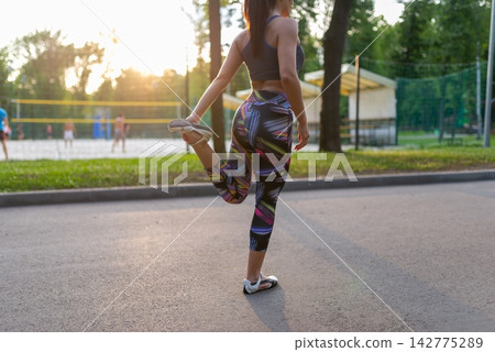 Woman stretching her quadriceps on a park path at sunset Woman stretching her quadriceps on a park path at sunset 142775289