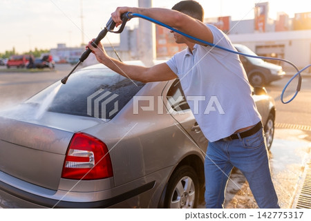 Man rinsing soapy rear window of silver sedan with pressure washer Man rinsing soapy rear window of silver sedan with pressure washer 142775317