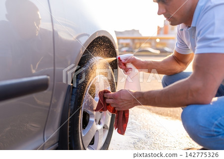 Man spraying chemical detergent on car tire and wiping rim Man spraying chemical detergent on car tire and wiping rim 142775326