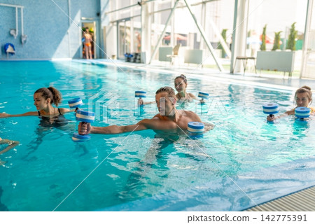 Group exercising with foam dumbbells in pool Group exercising with foam dumbbells in pool 142775391