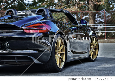 一輛黑色的保時捷981 Boxster Spyder跑車,像鏡子一樣映照著周圍的景色。 一輛黑色的保時捷981 Boxster Spyder跑車,像鏡子一樣映照著周圍的景色。 142775402