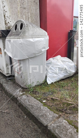 A dirty trash can and overflowing garbage bags placed next to a vending machine. A dirty trash can and overflowing garbage bags placed next to a vending machine. 142775495