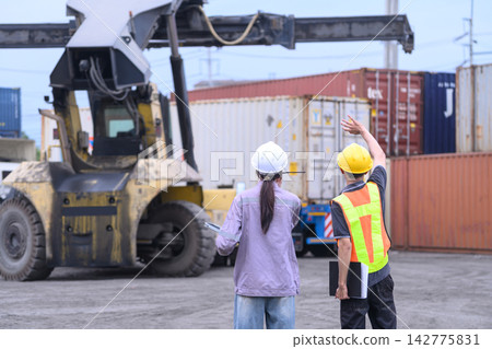 Shipping terminal staff coordinating heavy container transport and cargo movement operation. Shipping terminal staff coordinating heavy container transport and cargo movement operation. 142775831
